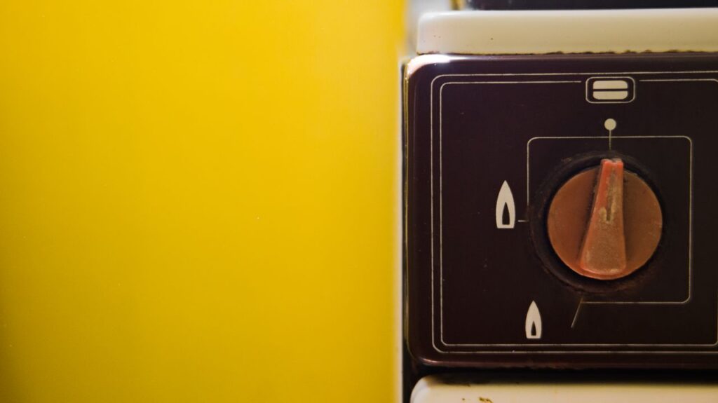 Close-up of a vintage gas stove knob on a vibrant yellow background.